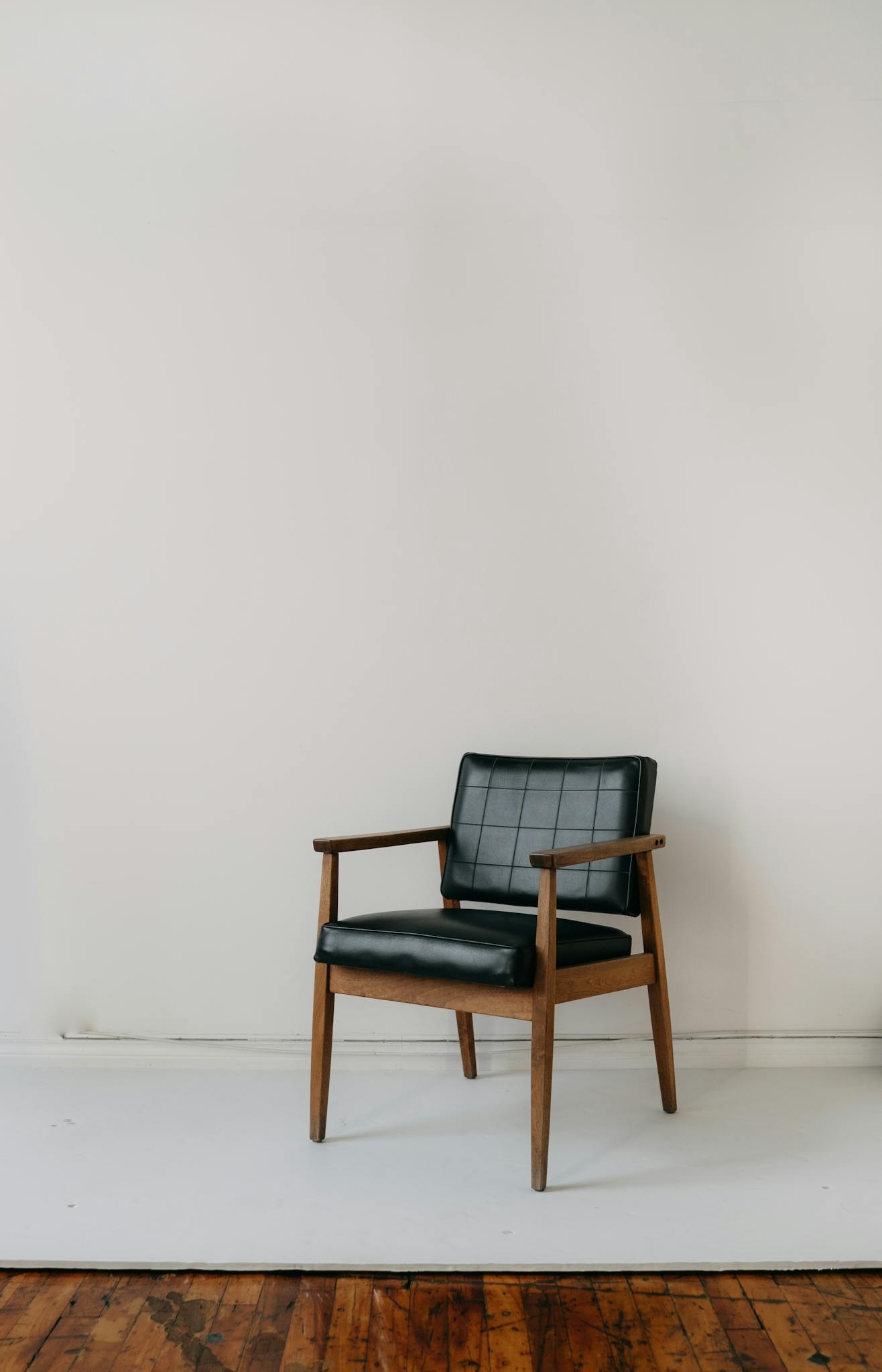 A vintage leather armchair placed against a plain wall in a minimalist indoor setting.